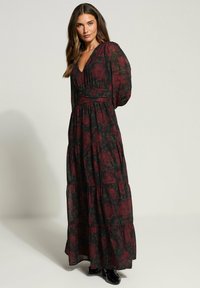 Robe maxi en tissu noir avec un motif floral rouge, présentant un col en V, un bodice froncé et de longues manches bouffantes. Design en niveaux et détail à la taille.