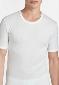 T-shirt bianca a maniche corte realizzata in morbido cotone. Presenta un collo rotondo con un bordo bianco a contrasto. Design semplice e attillato.