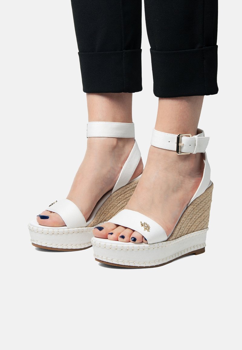 Sandalias de cuña blancas con un envoltorio de yute, tira para el tobillo ajustable, parte superior de tejido suave y un sutil detalle metálico en la tira frontal.
