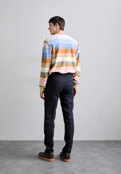 Sweater às riscas em cores pastel, calças escuras e sapatos castanhos. O sweater apresenta linhas horizontais e punhos canelados. Estilo casual.