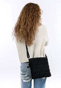 Borsa a spalla nera trapuntata con finitura testurizzata, cuciture a contrasto e tracolla regolabile, indossata in modo casual su un maglione chiaro e jeans.