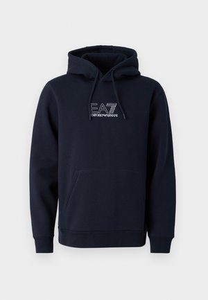 Haut à capuche bleu marine avec une poche kangourou à l'avant et un capuchon ajustable par cordon de serrage, associé à un pantalon cargo beige avec poches latérales et une coupe décontractée.