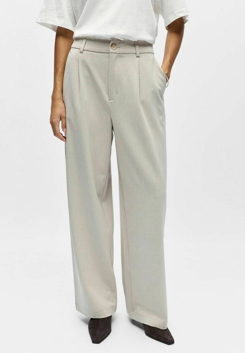 Pantalon beige à jambes larges avec une taille haute, deux poches latérales et une fermeture à bouton. Tissu doux avec une texture lisse et une coupe ajustée.