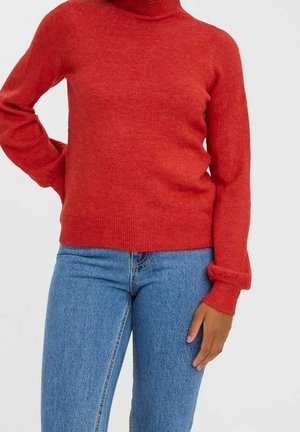 Pull col roulé rouge en tricot avec des manches longues, silhouette ajustée et ourlet côtelé. Associé à un jean en denim bleu, affichant un style décontracté.