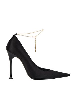 Zapato negro de tacón alto con punta afilada, tacón de aguja delgado y delicada cadena dorada en el tobillo, sobre fondo blanco.