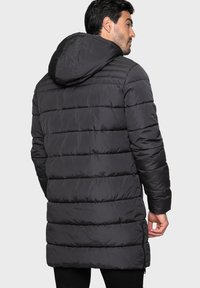 Mörk pufferjacka med huva, quiltat mönster och sidofickor. Tillverkad av ett smidigt, vattenavvisande material, perfekt för kalla väderförhållanden.