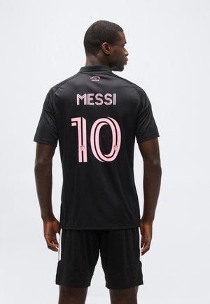 Férfi fekete labdarúgó-mezben és rövidnadrágban, a mez hátulján rózsaszínnel nyomtatva a "MESSI" felirat és a 10-es szám.