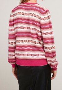 Pull en tricot avec un motif géométrique rose et blanc, des accents bruns, des poignets côtelés et un ourlet rose uni.