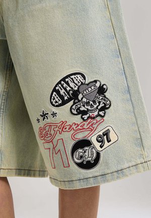 Light denim shorts with multiple embroidered patches, including a skull with heart and banner, stars, "Ed Hardy" text, and numbers "71" and "97".