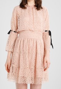 Abito in pizzo di un delicato rosa con maniche lunghe, vita arricciata, gonna svasata e dettagli in nastro nero sulle maniche. Presenta una texture in pizzo intricata.