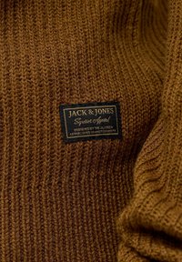 Brauner gestrickter Pullover mit gerippter Textur und einem schwarzen Etikett, auf dem "Jack & Jones" sowie die Produktdetails deutlich sichtbar sind.