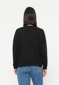 Zwarte sweatshirt met een ronde hals en verlaagde schouders, gecombineerd met lichtblauwe denim jeans, gezien vanaf de achterkant.