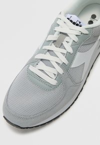 Baskets de sport gris clair en mesh et en daim, avec des lacets blancs, un col rembourré et une semelle extérieure en caoutchouc texturé.