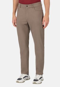 Beżowe elastyczne spodnie z pętlami na pasek, kieszeniami z przodu i dopasowanym krojem. Noszone z białymi i czarnymi masywnymi sneakersami.