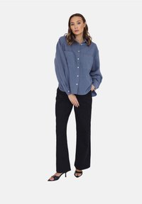 Niebieska koszula z guzikami z dwoma kieszeniami na piersi, zestawiona z czarnymi spodniami o szerokich nogawkach i czarnymi sandałami na obcasie. Gładka tekstura, luźny krój.