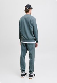 Donkergroene sweatshirt en bijpassende joggers van zacht materiaal, met ribbelmansjetten, zijvakken en zwarte sneakers met witte zolen.