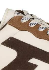Close-up van een witte sneaker met bruin suède accenten en witte veters met blauw en bruin geblokte patronen.