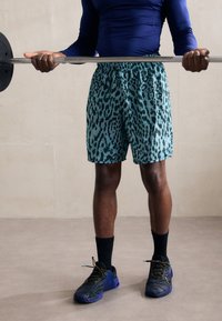 Turkiozo leopardų rašto šortai su elastinga juosta, derinami su juodais sportiniais batais ir ilgomis kojinėmis, laikomi pakeliant štangą.