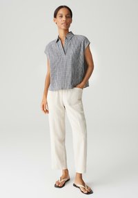 Blusa grigia a righe senza maniche in misto cotone con colletto, abbinata a pantaloni larghi color crema e infradito neri, il tutto su uno sfondo neutro.