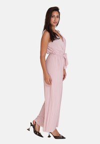 Lange, geplooide jumpsuit van zachtroze stof, met een wikkelontwerp en een strikceintuur in de taille. Gecombineerd met glanzende zwarte pumps.