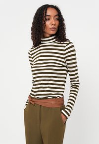 Langermet turtleneck med grønne og hvite horisontale striper, laget av myk stoff, kombinert med høytlivte olivengrønne bukser og et brunt belte.