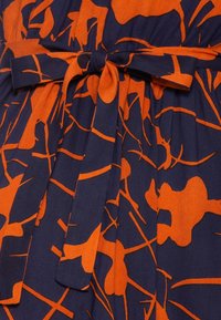 Marinblått tyg med ett orange abstrakt mönster med varierande former, accentuerat av ett matchande tygbälte som är knutet i midjan.