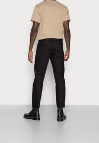 Black jeans with a slim fit, featuring standard back pockets, paired with a beige t-shirt and black chelsea boots on a gray surface.