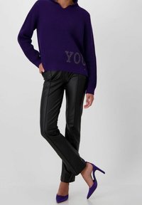 Maglione viola lavorato a maglia con scollo a V e dettaglio di strass, abbinato a pantaloni neri in similpelle e décolleté viola.