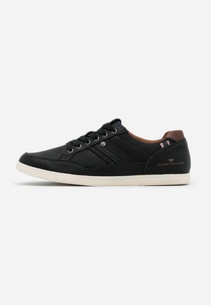 Black casual sneakers with textured upper, white rubber sole, and contrasting brown accents on the heel. Features round laces and stitched details.