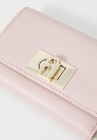 Pink textured leather wallet with a gold hardware clasp and a rectangular design. Features visible stitching along the edges.