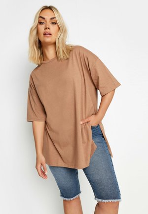 Camiseta marrón de gran tamaño con mangas cortas, que presenta aberturas en los laterales, combinada con shorts de mezclilla de tiro medio con dobladillo deshilachado. Textura suave.