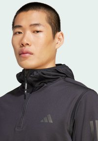 Schwarze Laufjacke mit durchgehendem Reißverschluss und hohem Kragen, mit strukturiertem Muster und dezenten Logo-Details. Glatter Stoff mit eng anliegender Passform.