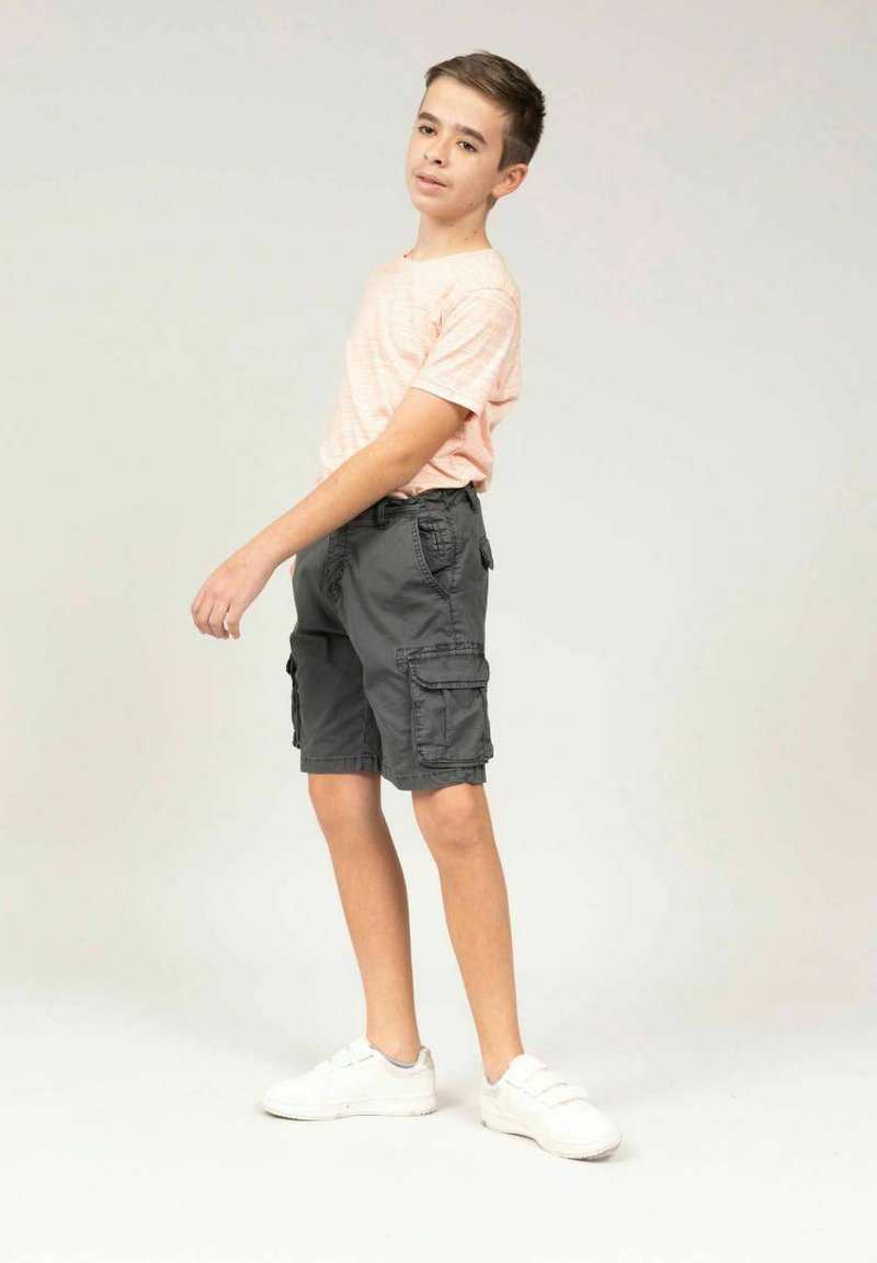 T-shirt rayé rose clair, shorts cargo gris avec plusieurs poches, et sneakers blancs. Design simple et coupe décontractée.