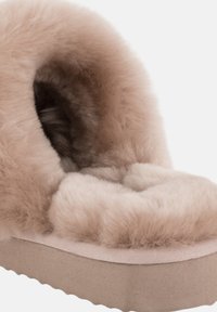 Ljusbeige, fluffig toffel med plyschinredning, rund tå och mjuk textur. Tjock sula med ett subtilt mönster. Utformad för komfort och värme.