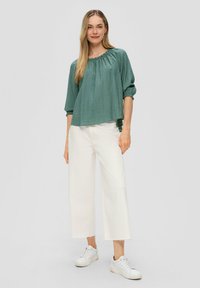 Losse teal lange mouw top met een geraffineerde halslijn, gecombineerd met witte wijde jeans en witte sneakers. Zachte stof met een subtiele textuur.