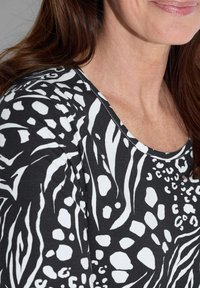 Zwart-wit top met een gestructureerd, dierenprintpatroon met verschillende vormen. De halslijn is rond en de stof lijkt zacht te zijn.