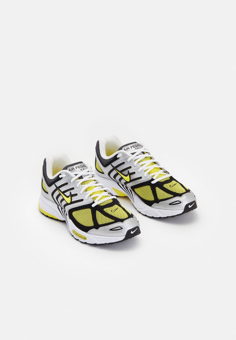 Fekete és sárga sportcipők hálós felsőrésszel, visszaverő részletekkel és fehér talppal. Jellemzője egy feltűnő Nike logó az oldalon.