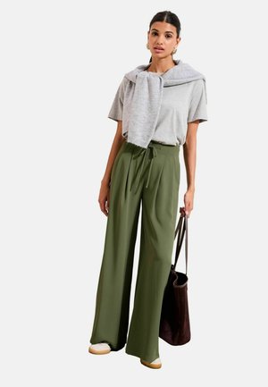 Zöld, széles szárú nadrág, derékrészén megkötővel, hozzá szürke póló és vállra terített világosszürke sál. Barna válltáska.