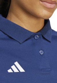 Polo blu navy realizzato in tessuto testurizzato, dotato di colletto, due bottoni e un logo ricamato bianco con tre strisce a sinistra.