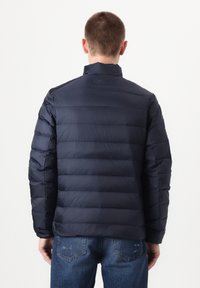 Zilganpelēka pūkaina jaka ar kvadrātdūrienu dizainu, augstu apkakli un rāvējslēdzēja aizdari, kombinēta ar gaiši zilām džinsu biksēm. Gluda un plūstoša tekstūra.