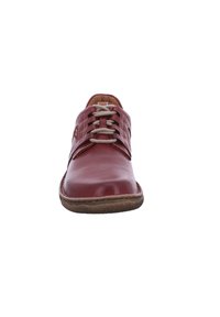 Zapato de cuero rojo con puntera redondeada, que presenta cordones grises y detalles de costura. La suela es plana y ligeramente texturizada.