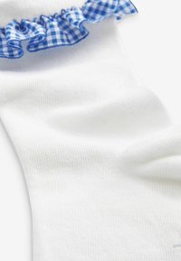 Calzino bianco in cotone con texture a coste e un accento arricciato in gingham blu sulla parte superiore. Il tessuto liscio si estende verso il basso in una forma aderente.