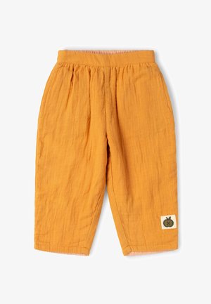 Locker sitzende, senfgelbe Baumwollhose mit elastischem Bund und einem kleinen grünen Apfelpatch nahe dem unteren Saum am rechten Bein.