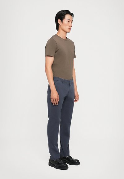Khaki kortärmad skjorta, marinblå byxor med en subtil textur och svarta loafers. Enkelt, figurnära design med rena linjer och en klassisk stil.