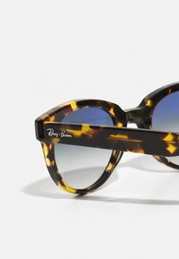 Occhiali da sole Ray-Ban in tartaruga con lenti arrotondate e sfumatura blu. Presentano una montatura spessa e il logo del marchio ben visibile sul braccio.