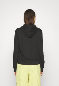 Czarna bluza z kapturem, o miękkiej fakturze i prążkowanych mankietach. Tył jest gładki, bez wzorów, w zestawie z jasnobrązowymi spodniami cargo.