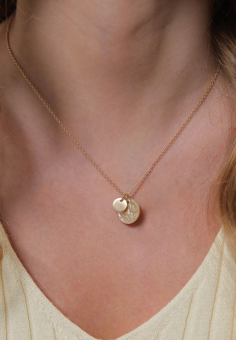 Collier en or avec deux pendentifs : l'un rond, lisse et poli ; l'autre plus petit, texturé avec un motif subtil. La chaîne est délicate.