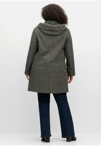 Grijze houndstooth jas met een gedrapeerde kraag, lange mouwen en een rechte snit, gedragen met donkerblauwe flared jeans en zwarte laarzen.