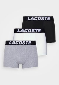 Trei perechi de boxeri pentru bărbați în gri, alb și negru, cu un elastic negru ce are inscripționat "LACOSTE" în litere albe.
