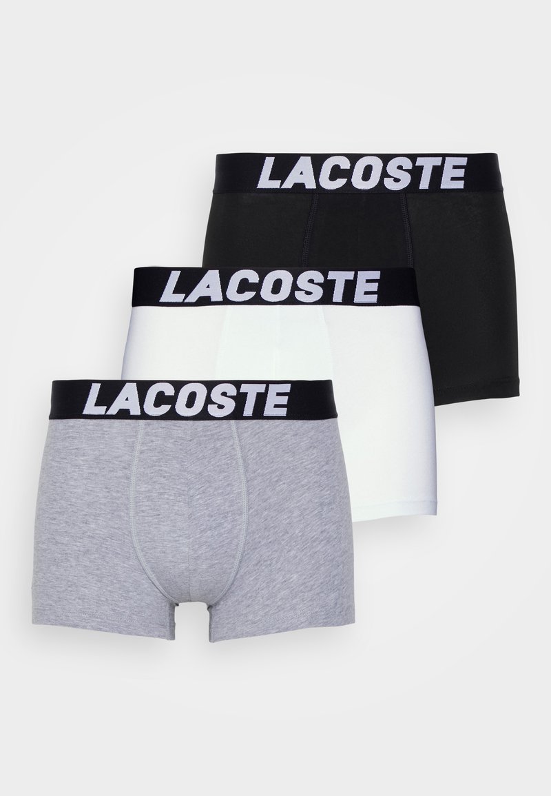 Tre par herrboxershorts i grått, vitt och svart, med en svart midja med "LACOSTE" i vit text.